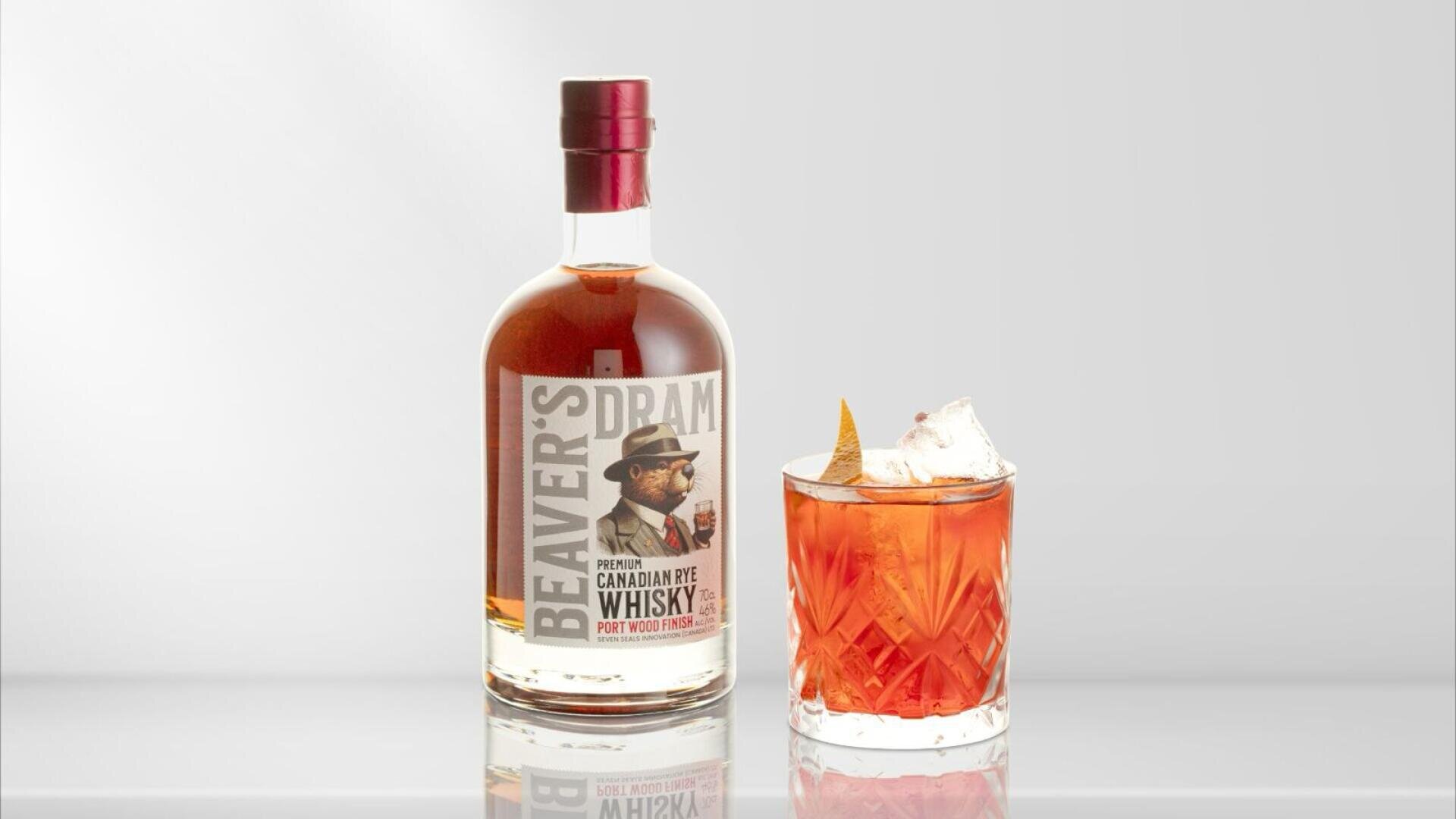 Une bouteille de Beavers Dram Canadian Rye Whisky est posée à côté d'un verre de cocktail de whisky avec de la glace et un twist à l'orange, sur un fond sobre et clair.