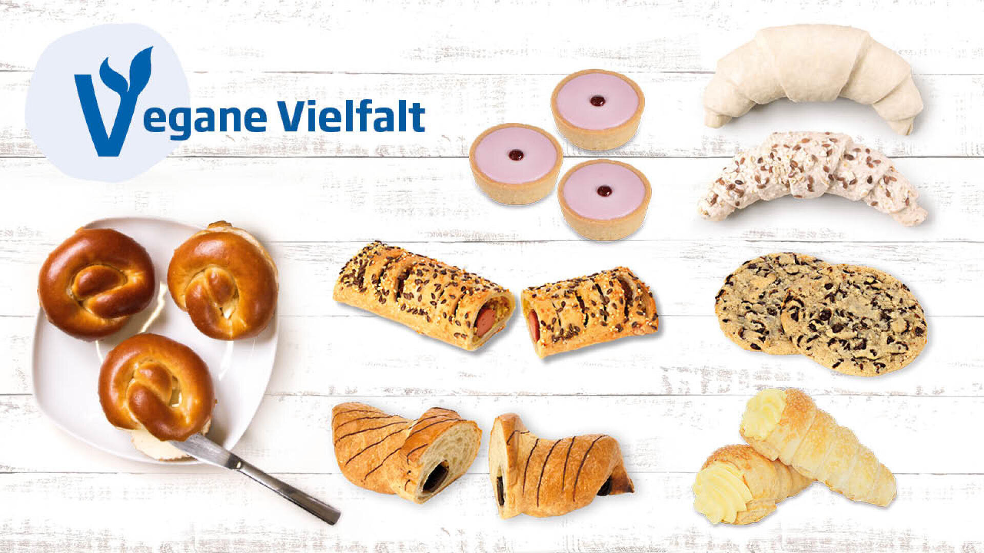 Auf einer weißen Holzfläche mit dem Schriftzug Vegane Vielfalt und einem blauen Vegan-Logo in der linken oberen Ecke werden verschiedene vegane Backwaren wie Brezeln, Gebäck, Kekse und Brötchen angeboten.