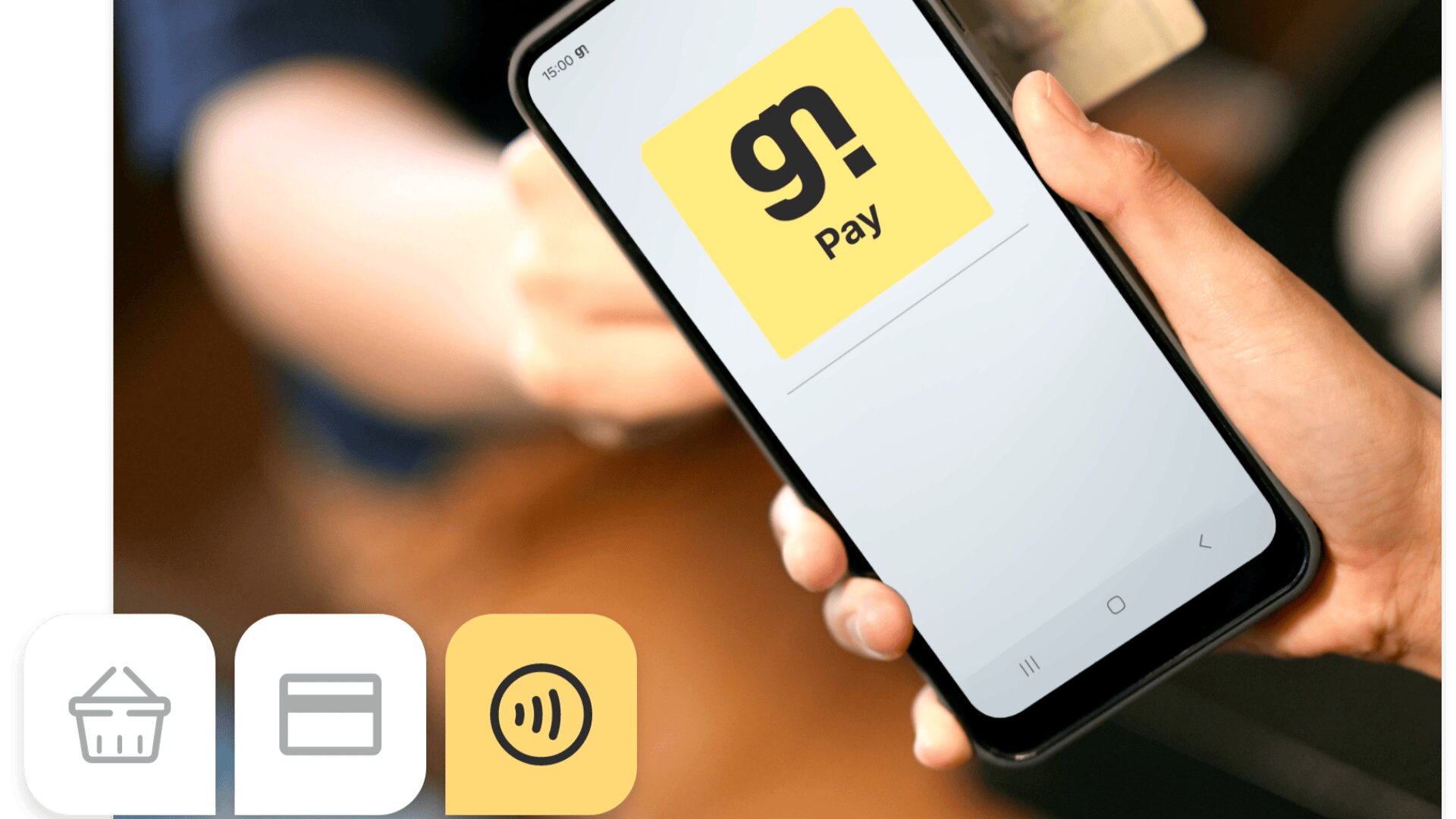 Eine Person hält ein Smartphone mit der gn! Pay-App und bereitet sich auf eine kontaktlose Zahlung vor. Drei Symbole - Warenkorb, Kreditkarte und kontaktlose Zahlung - sind unten links zu sehen.