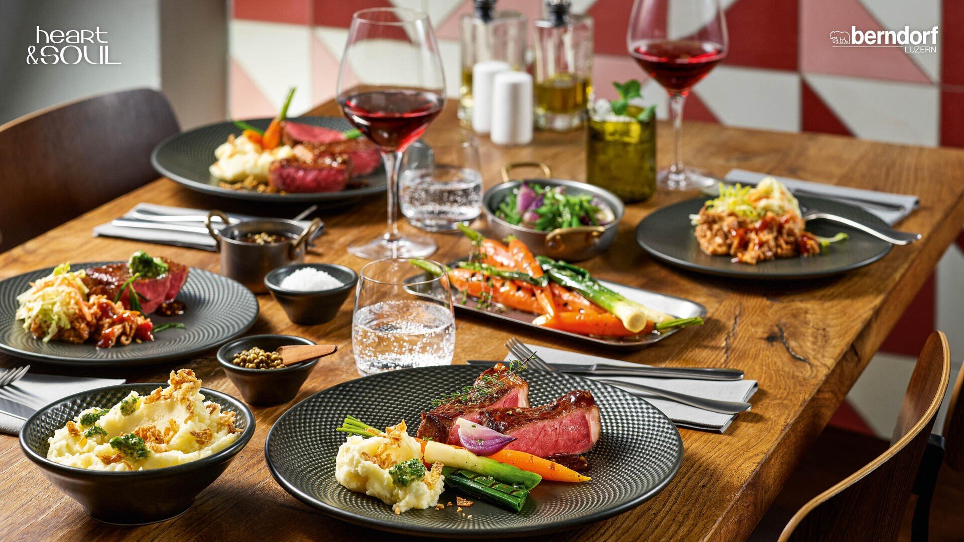 Ein Holztisch für vier Personen mit Gourmet-Essen auf Tellern, buntem Gemüse, einem Steak, mit Rotwein gefüllten Weingläsern, Wassergläsern und Utensilien schafft eine elegante Essatmosphäre.