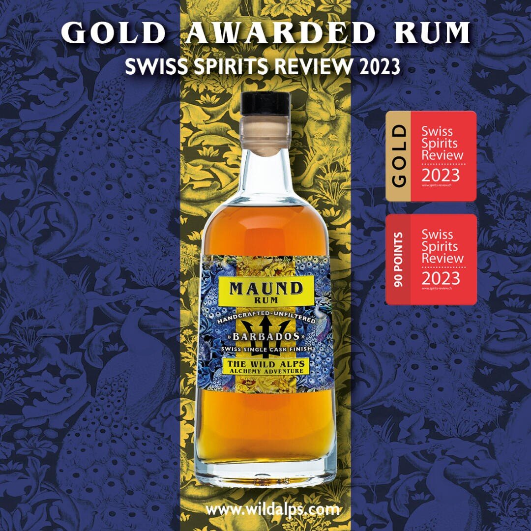 L'illustration représente une bouteille de rhum Maund avec une étiquette bleue et dorée. Le texte indique "Gold Awarded Rum, Swiss Spirits Review 2023", avec des distinctions dorées et rouges à côté de la bouteille. Des motifs ornementaux bleus et or sont visibles en arrière-plan.