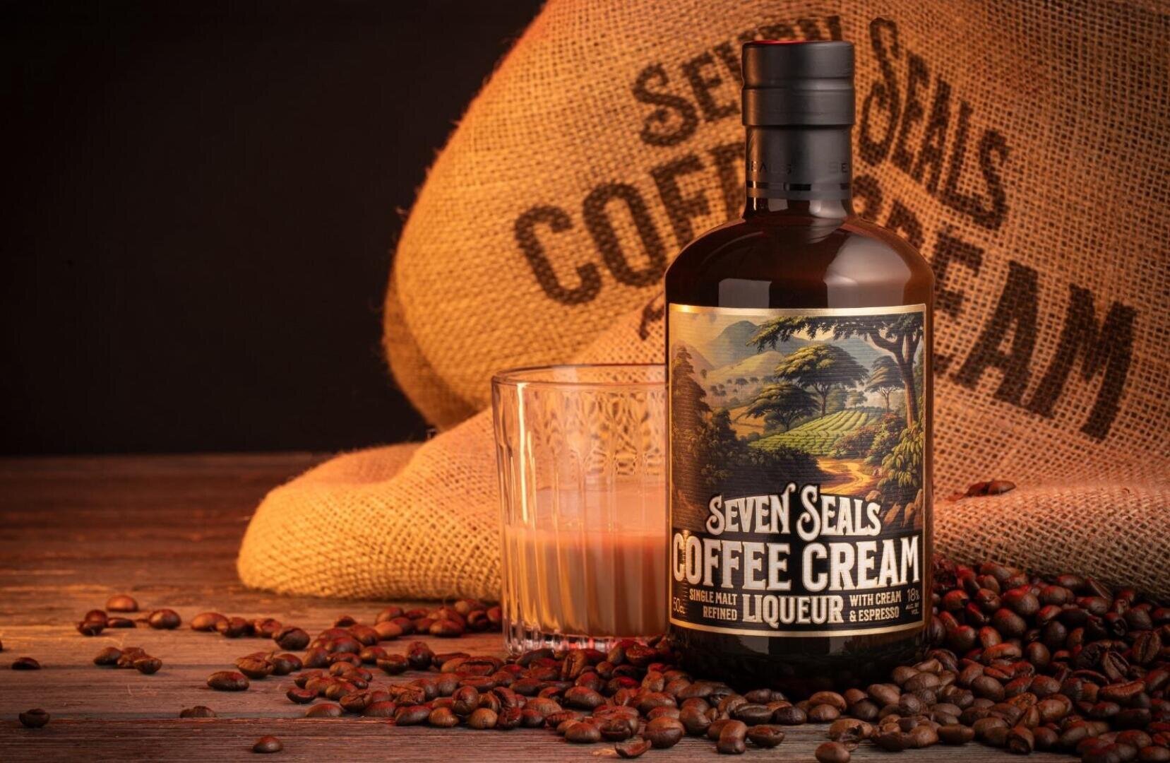 Une bouteille de Seven Seals Coffee Cream Liqueur est posée à côté d'un verre rempli de la boisson, entourée de grains de café et d'un sac en toile de jute portant l'inscription COFFEE CREAM en arrière-plan.