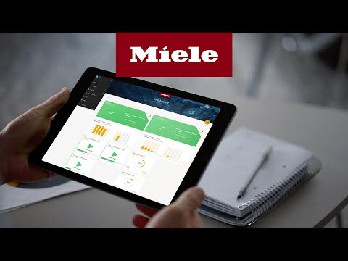 Eine Person hält ein Tablet mit Diagrammen und Grafiken in der Hand, daneben liegt ein Spiralblock mit Stift auf einem Schreibtisch. Das Miele-Logo ist am oberen Rand des Bildes prominent platziert.