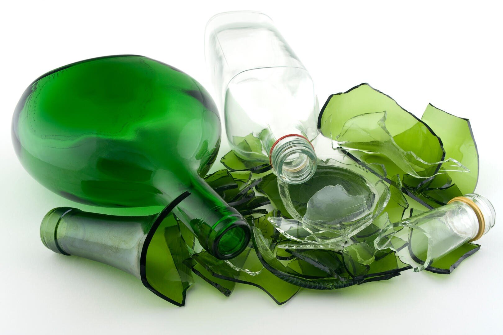 Deux bouteilles en verre, l'une verte et l'autre transparente, sont posées au milieu de grands morceaux de verre vert sur une surface blanche. Les bouteilles sont vides et les morceaux de verre sont éparpillés autour d'elles.