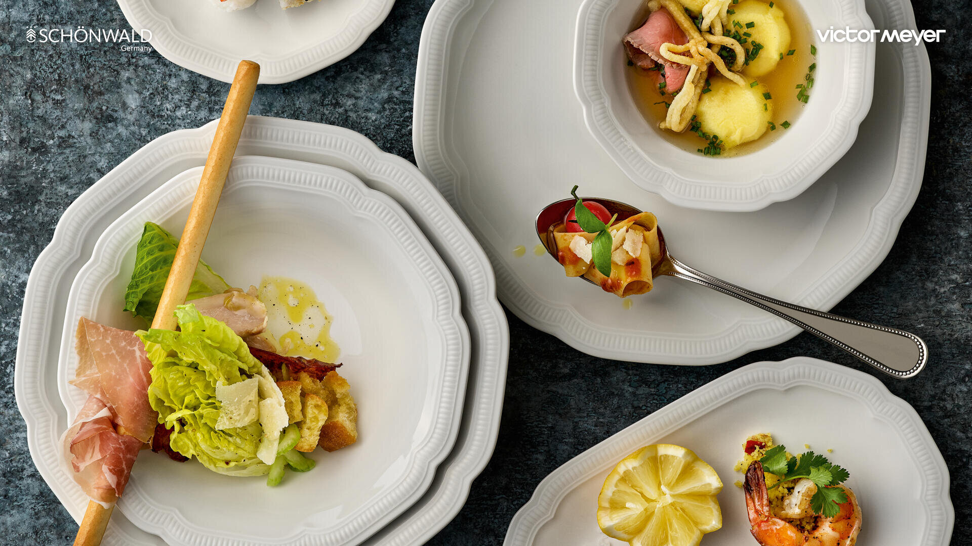 Eine Vielzahl von Gourmetgerichten, die auf eleganten weißen Tellern serviert werden, darunter Salat mit Prosciutto, gefüllte Nudeln in Brühe, eine gerollte Vorspeise, Garnelen mit Kräutern und Zitronenscheiben, die auf einer dunkel strukturierten Oberfläche angeordnet sind.