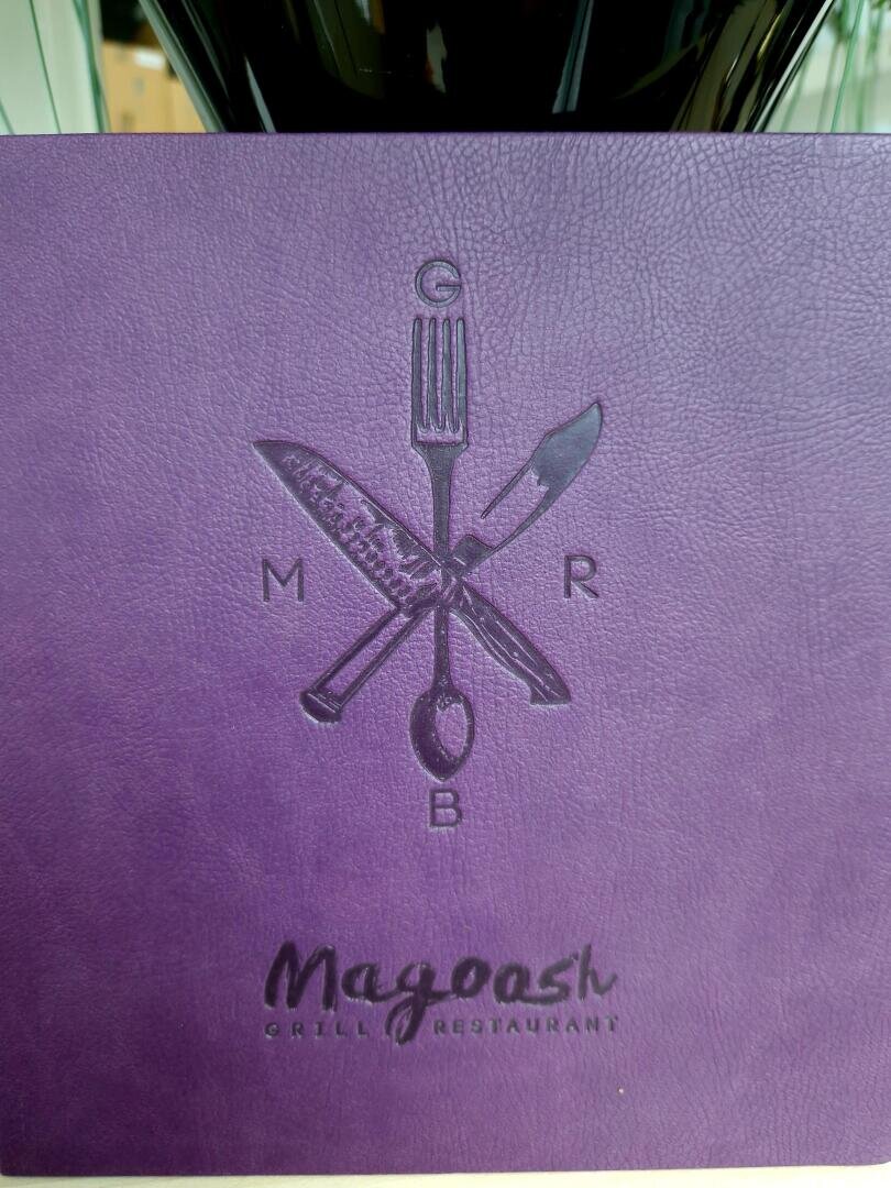 Auf der violetten, strukturierten Speisekarte ist das Besteck in Form eines Kreuzes geprägt, dazwischen die Buchstaben G, M, R und B und darunter der Schriftzug Mayoosh Grill Restaurant.