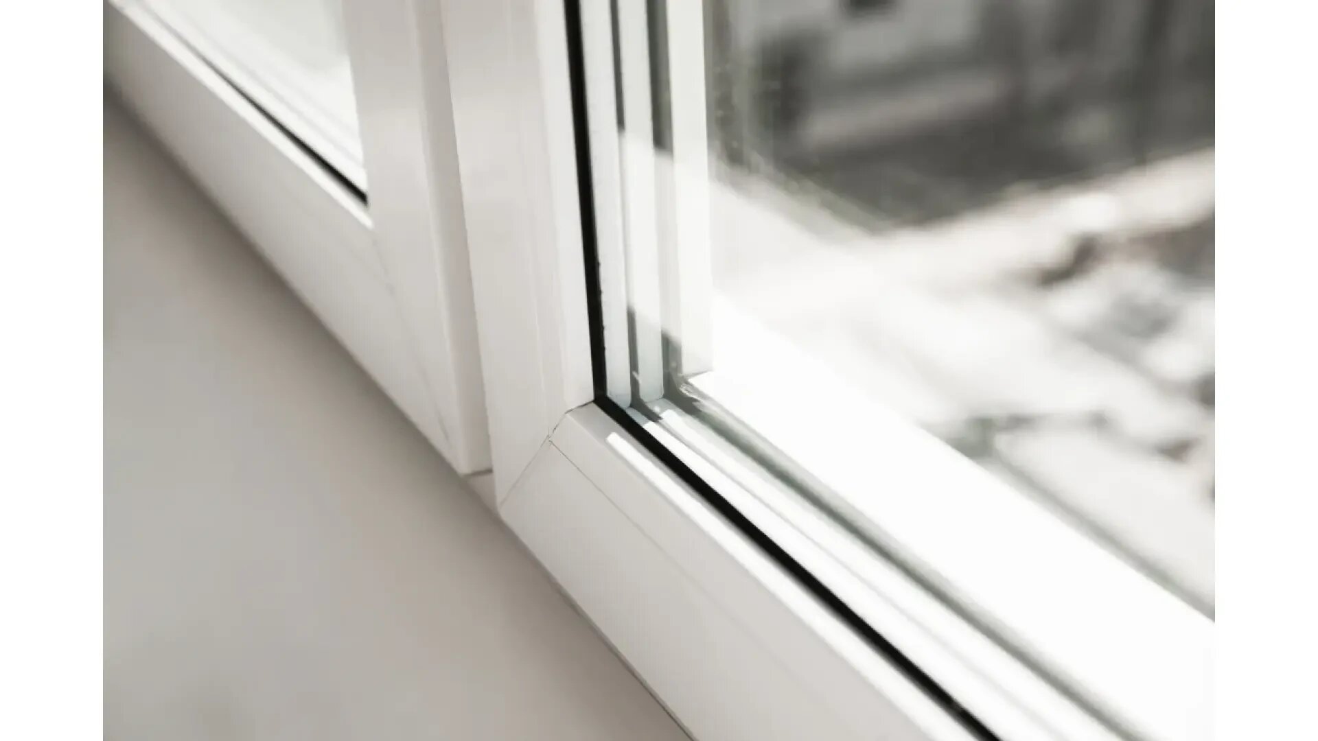 Nahaufnahme eines modernen, weiß gerahmten Fensters mit Doppelverglasung und Spiegelungen auf dem Glas, mit einem Teil der Fensterbank und einer unscharfen Außenlandschaft im Hintergrund.