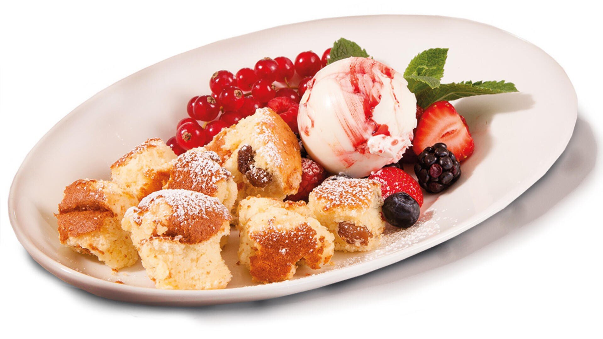 Ein weißer Teller mit Kuchenstücken, die mit Puderzucker bestäubt sind, eine Kugel Vanilleeis mit Beerensoße und verschiedene frische Beeren wie Erdbeeren, Johannisbeeren, Heidelbeeren und Brombeeren.