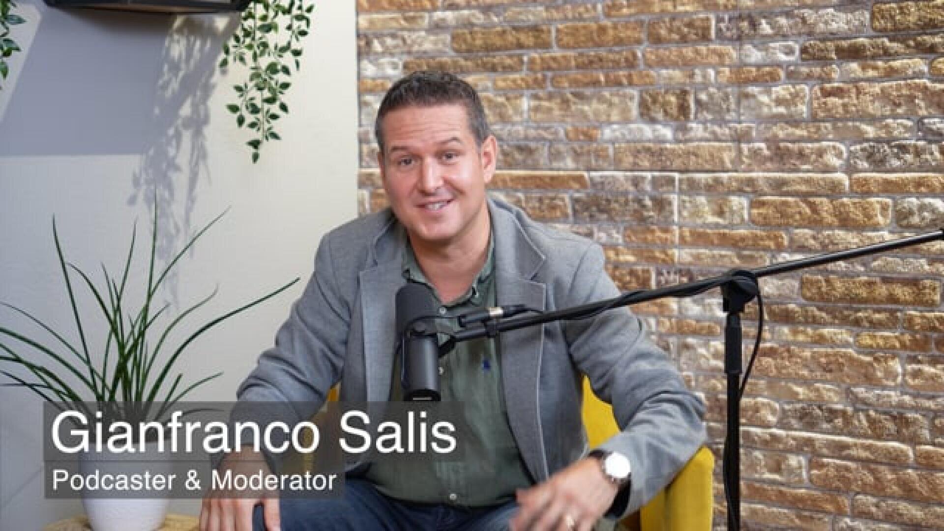 Un homme vêtu d'un blazer gris est assis sur une chaise jaune, il sourit et a un micro devant lui. Le texte sur l'image est Gianfranco Salis, podcaster & animateur. En arrière-plan, on peut voir un mur de briques exposé et des plantes.