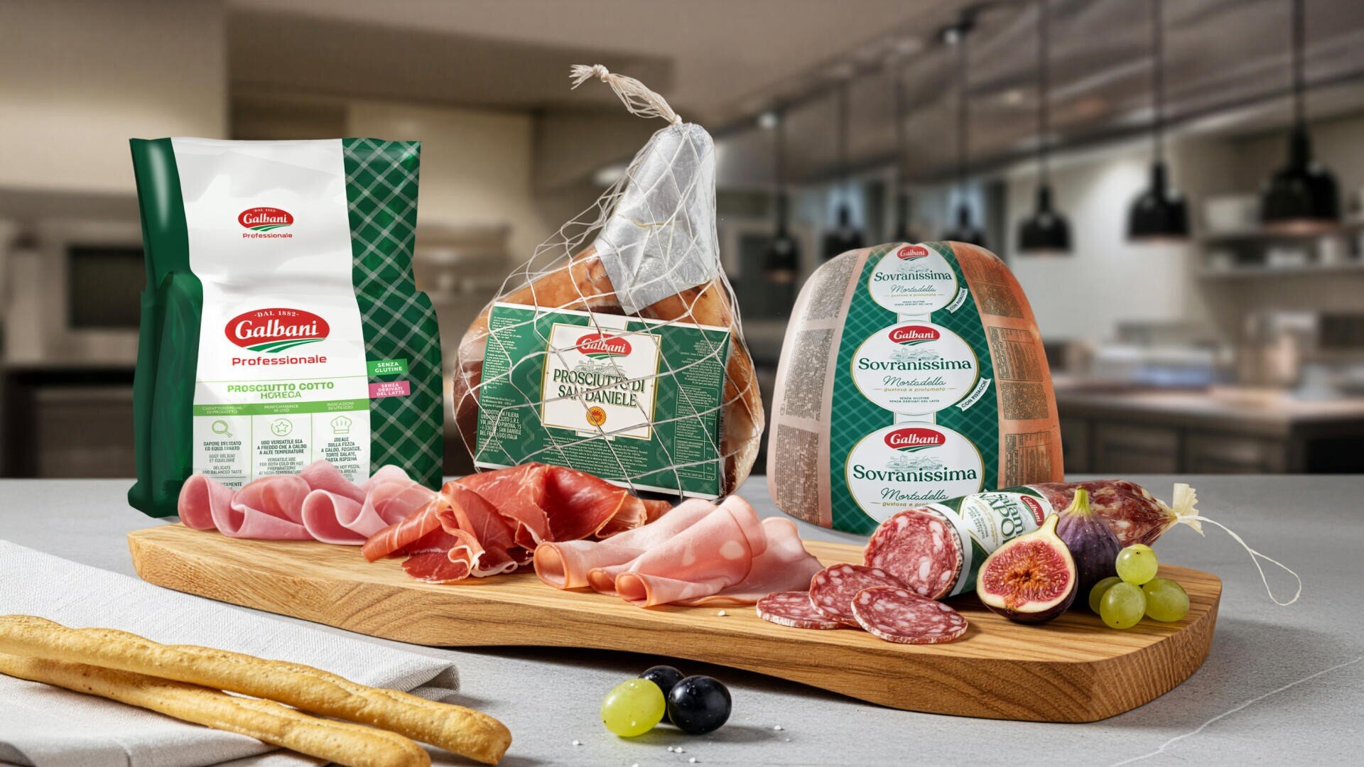 Ein Holzbrett mit verschiedenen italienischen Aufschnittarten, darunter Prosciutto, Salami und Mortadella, liegt auf einem Tisch mit geschnittenen Feigen, Trauben und Brotstangen; im Hintergrund sind in einer modernen Küche verschiedene verpackte Fleischsorten ausgestellt.
