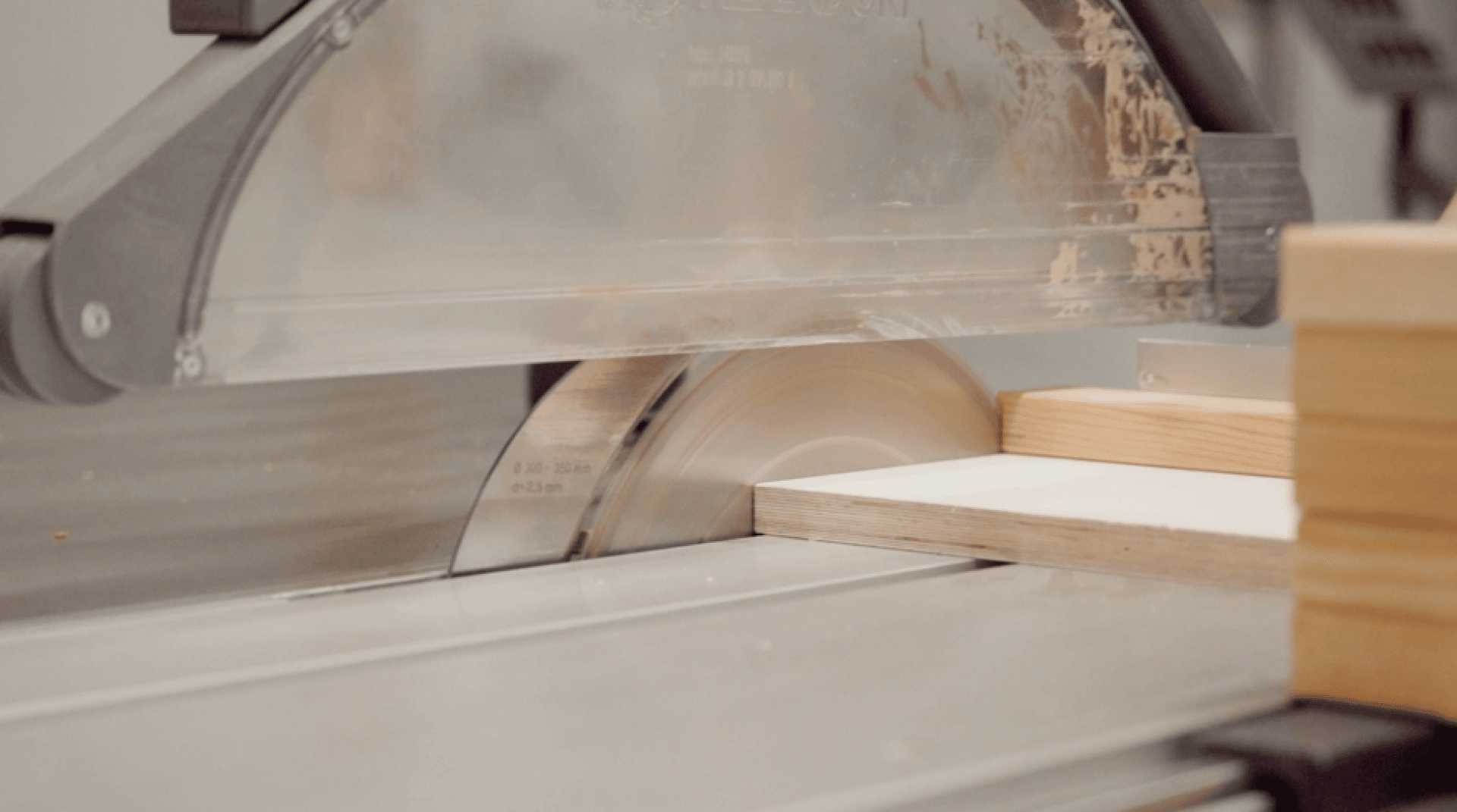 Nahaufnahme einer Kreissäge, die auf einer Werkbank ein Holzstück durchschneidet. Das Sägeblatt ist in Bewegung, und Holzstücke sind neben dem Schnittbereich positioniert.