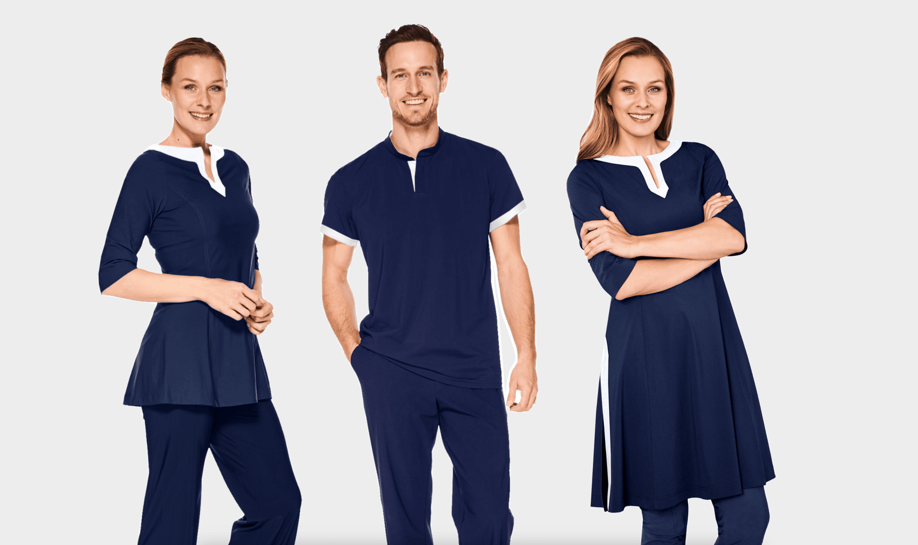 Drei Models stehen vor einem schlichten Hintergrund und tragen marineblaue Kleidung mit weißen Akzenten. Zwei Frauen tragen Tuniken und Hosen, während ein Mann in der Mitte ein kurzärmeliges Hemd und eine Hose trägt. Alle lächeln.