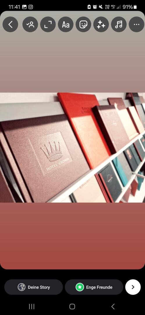 Mehrere gebundene Bücher und Ordner, darunter ein auffälliger roter Ordner mit der Aufschrift Hotel Crown und einem Kronenlogo, sind ordentlich auf weißen Regalen angeordnet. Das Foto ist schräg aufgenommen.