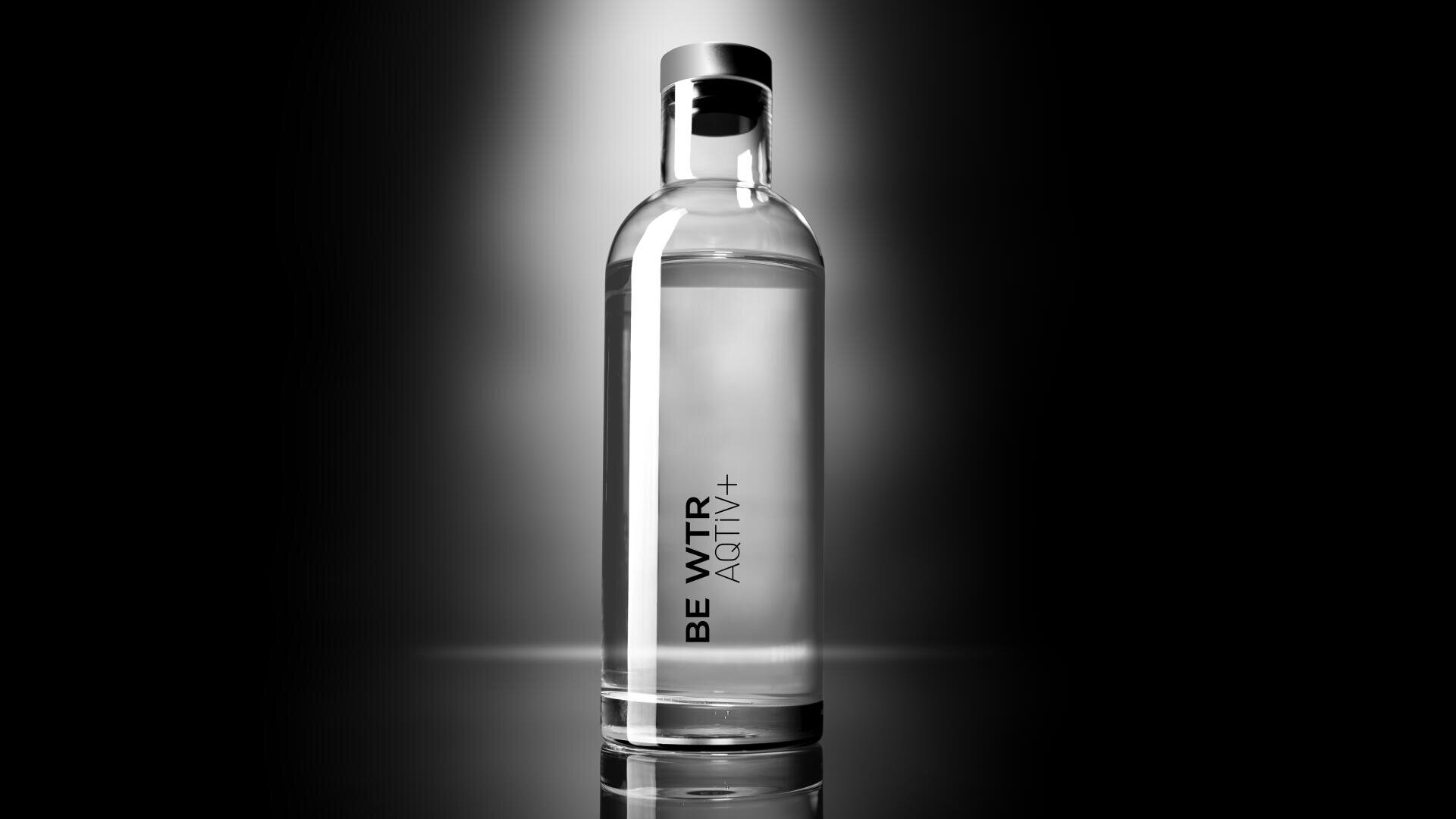 Une bouteille en verre transparent remplie d'eau se tient debout sur un fond noir et blanc spectaculaire, avec le texte BE WTR AQTiV+ à la verticale sur le devant de la bouteille.