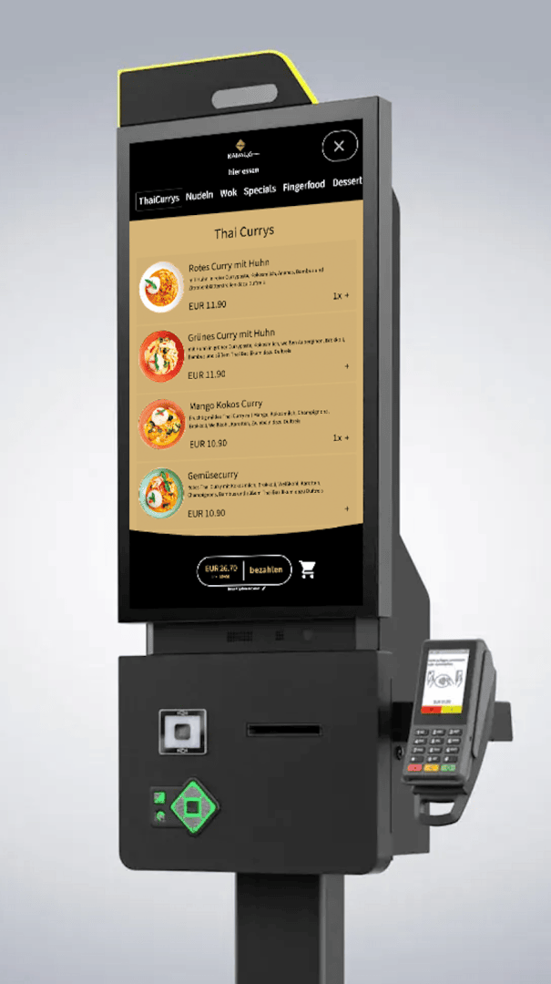 Ein Selbstbedienungskiosk mit Touchscreen zeigt eine Speisekarte mit Thai-Curry-Gerichten, Preisen und Bildern an. Unter dem Bildschirm sind ein Kartenzahlungsterminal und ein Belegdrucker angebracht.