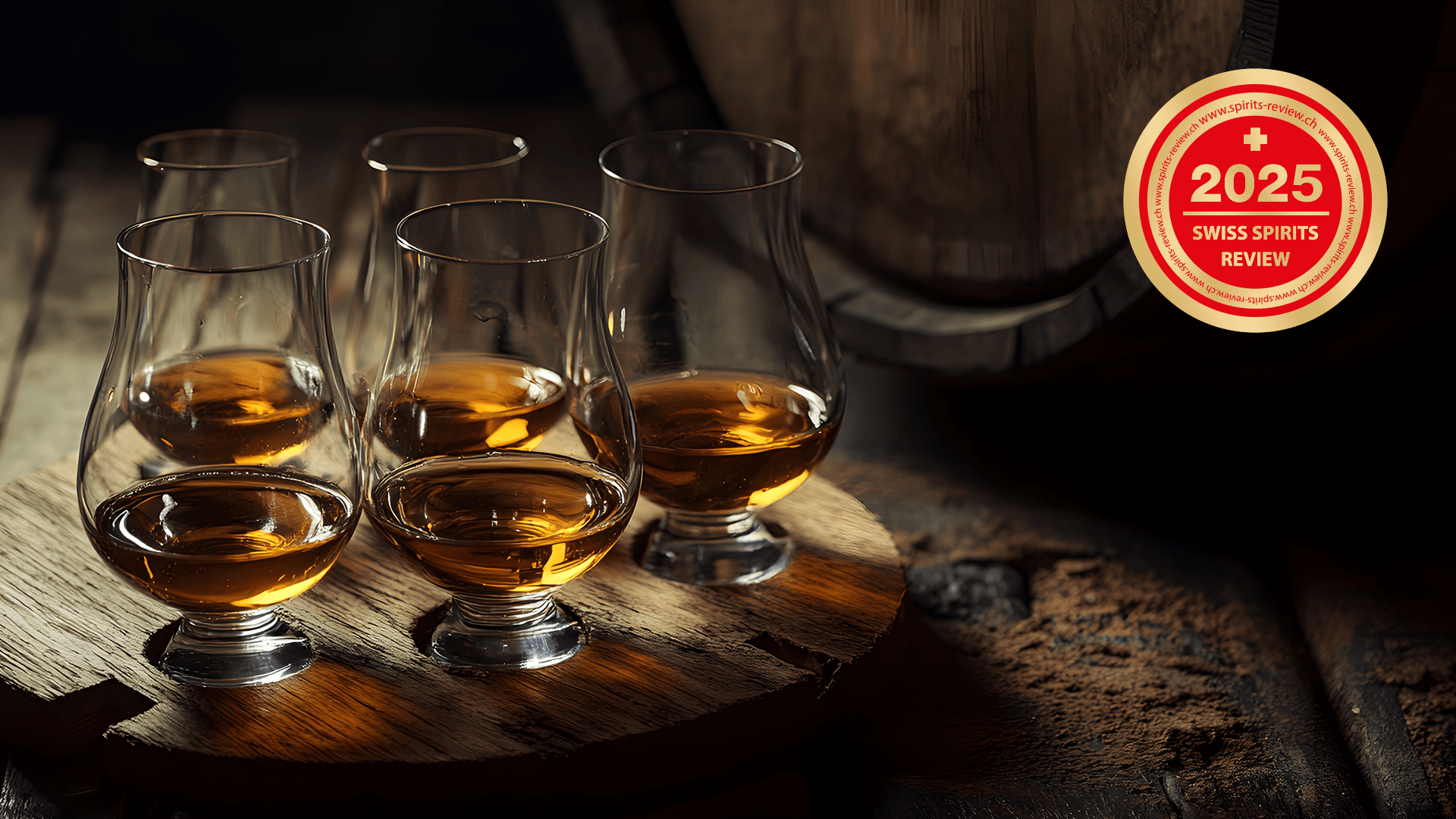 Fünf mit einer bernsteinfarbenen Flüssigkeit gefüllte Whiskygläser stehen auf einer Holzfläche neben einem Fass. In der oberen rechten Ecke ist ein rot-goldener Anstecker "2025 Swiss Spirits Review" zu sehen.