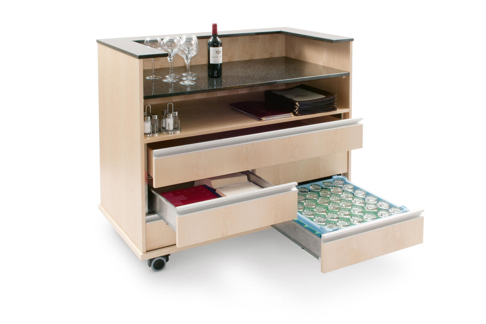 Un chariot de bar en bois clair avec un plan de travail foncé, qui contient des verres à vin, une bouteille de vin, des salières et des poivrières, trois tiroirs (dont un ouvert avec des gobelets en verre) et des étagères avec des plateaux et des assiettes, et qui est mobile grâce à des roulettes.