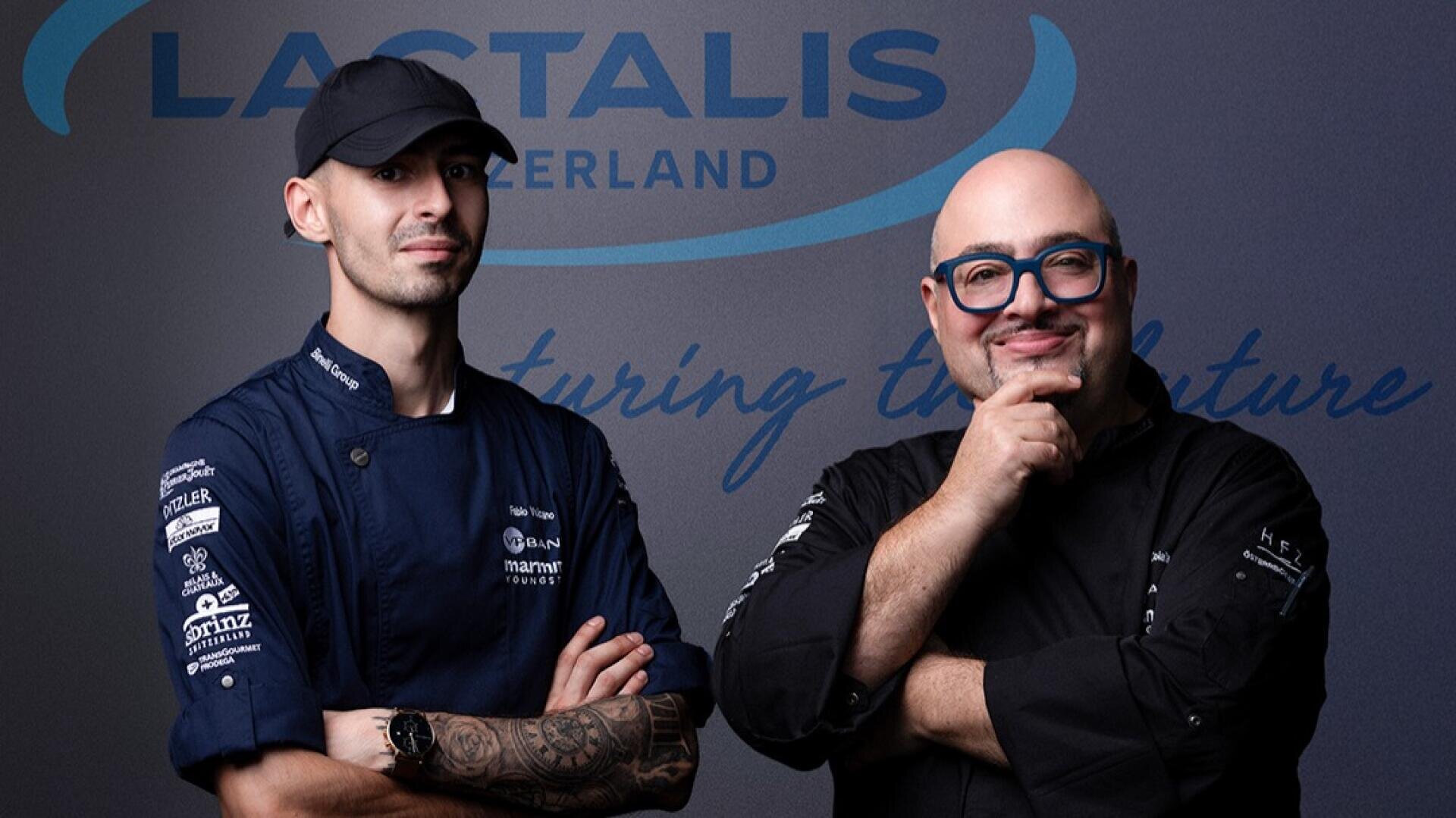 Zwei Köche in dunklen Uniformen stehen selbstbewusst lächelnd nebeneinander vor einer Wand mit dem Logo von Lactalis Schweiz und dem Slogan "Nurturing the Future".