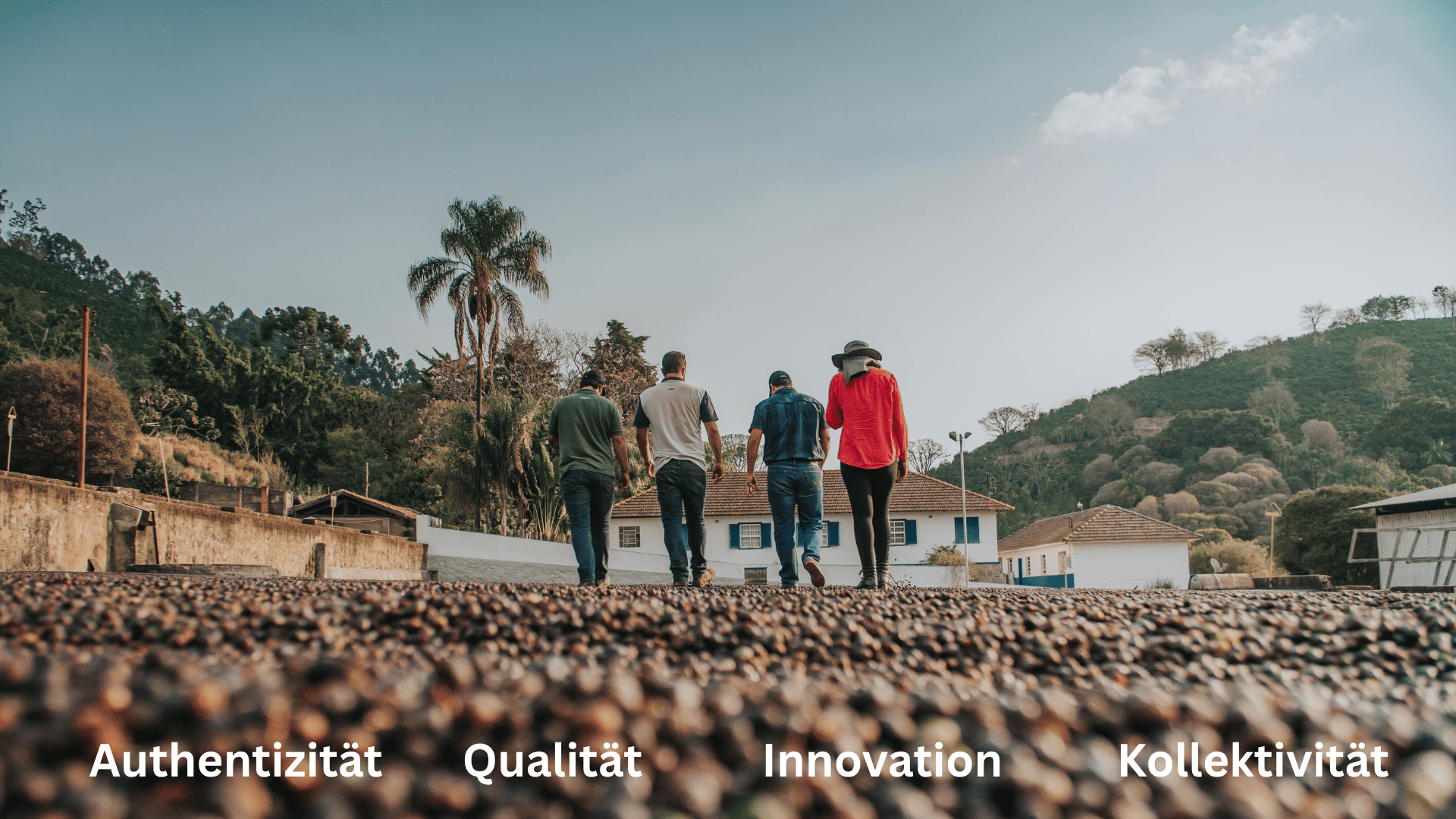 Vier Personen gehen gemeinsam auf einem Kiesweg in Richtung Häuser und grüner Hügel unter einem blauen Himmel. Am unteren Rand stehen die Worte Authentizität, Qualität, Innovation und Kollektivität.