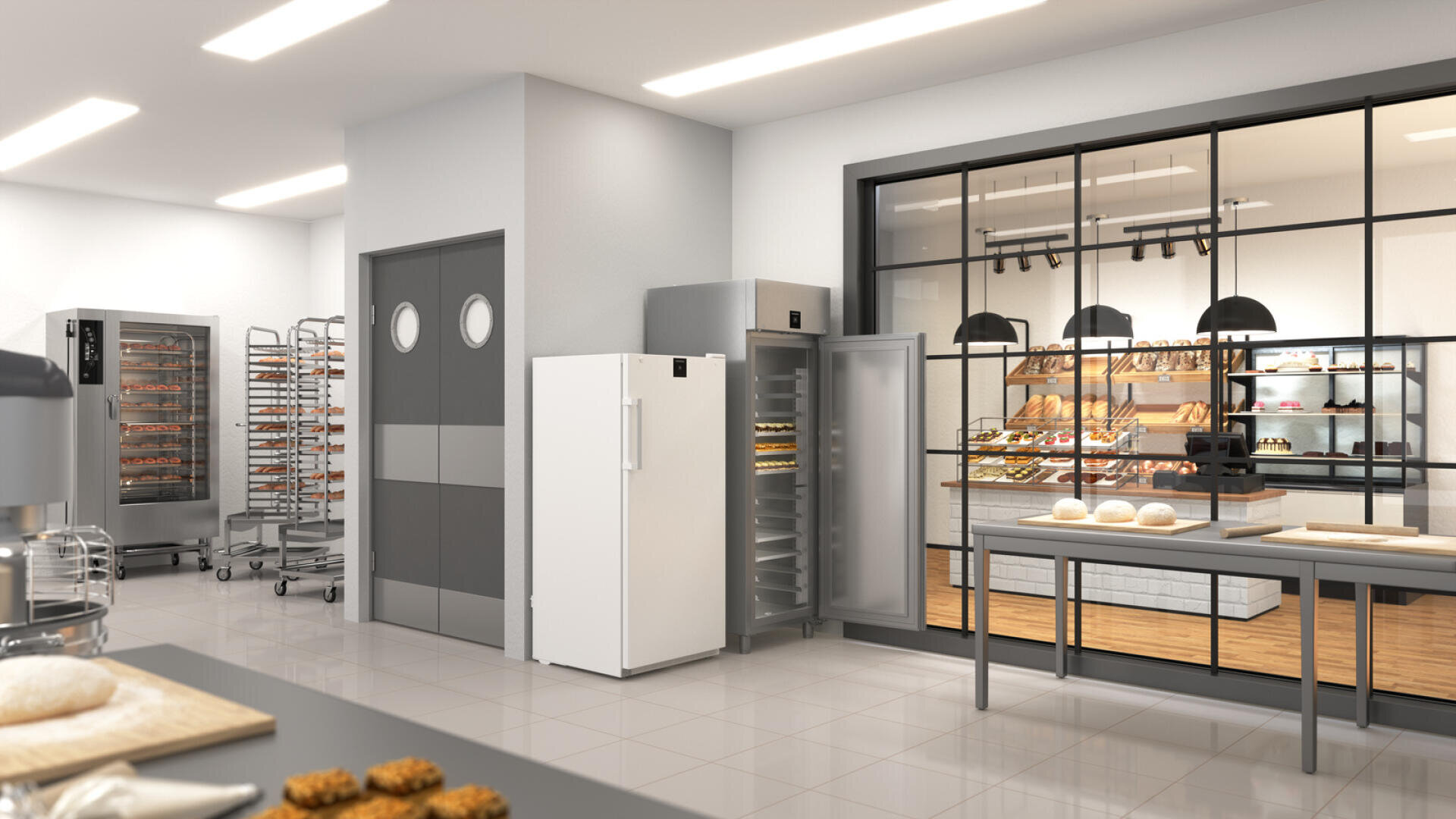 Eine moderne gewerbliche Bäckereiküche mit Geräten aus Edelstahl, Regalen mit Backblechen und einem Kühlschrank. Durch ein großes Fenster ist ein Ausstellungsbereich mit Regalen mit Backwaren zu sehen. Auf den Tischen liegen Teig und Brot.