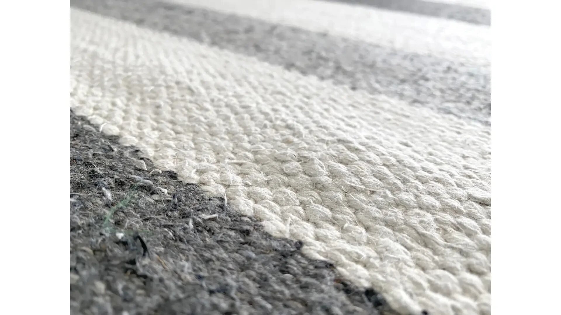 Nahaufnahme eines strukturierten Teppichs mit abwechselnd breiten, horizontalen Streifen in Creme- und Grautönen, die die gewebten Fasern im Detail zeigen.