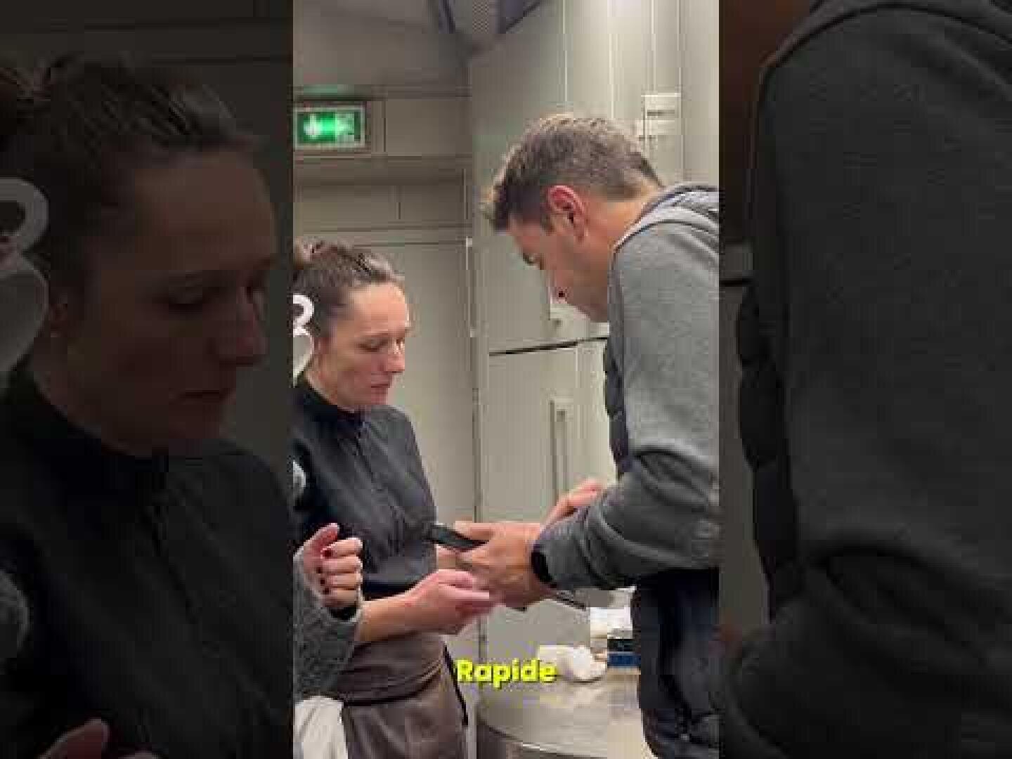 Zwei Personen stehen in einer Küche und führen ein konzentriertes Gespräch. Eine Frau hält einen Gegenstand, während der Mann ein Telefon betrachtet oder benutzt. Das Wort Rapide erscheint am unteren Rand des Bildes.