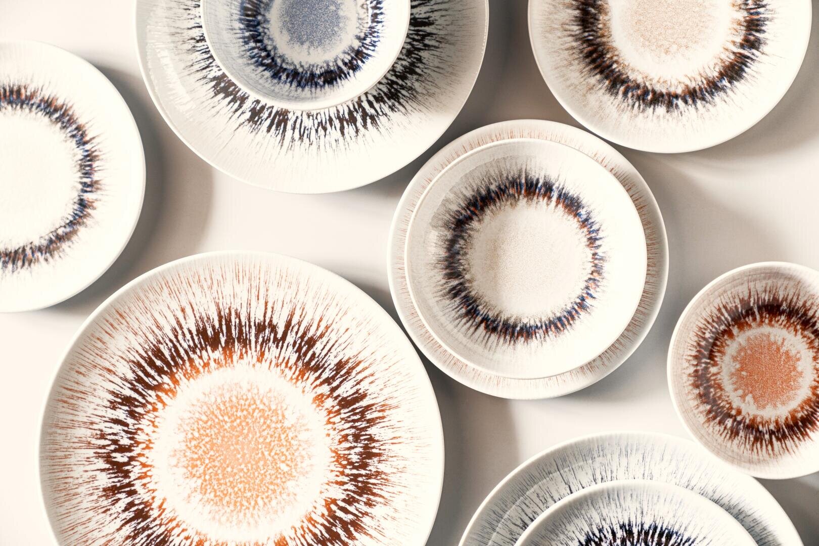 Différentes assiettes en céramique aux motifs radiaux de soleil dans des tons de marron, de bleu et de beige sont disposées sur une surface blanche, créant un affichage artistique et symétrique.