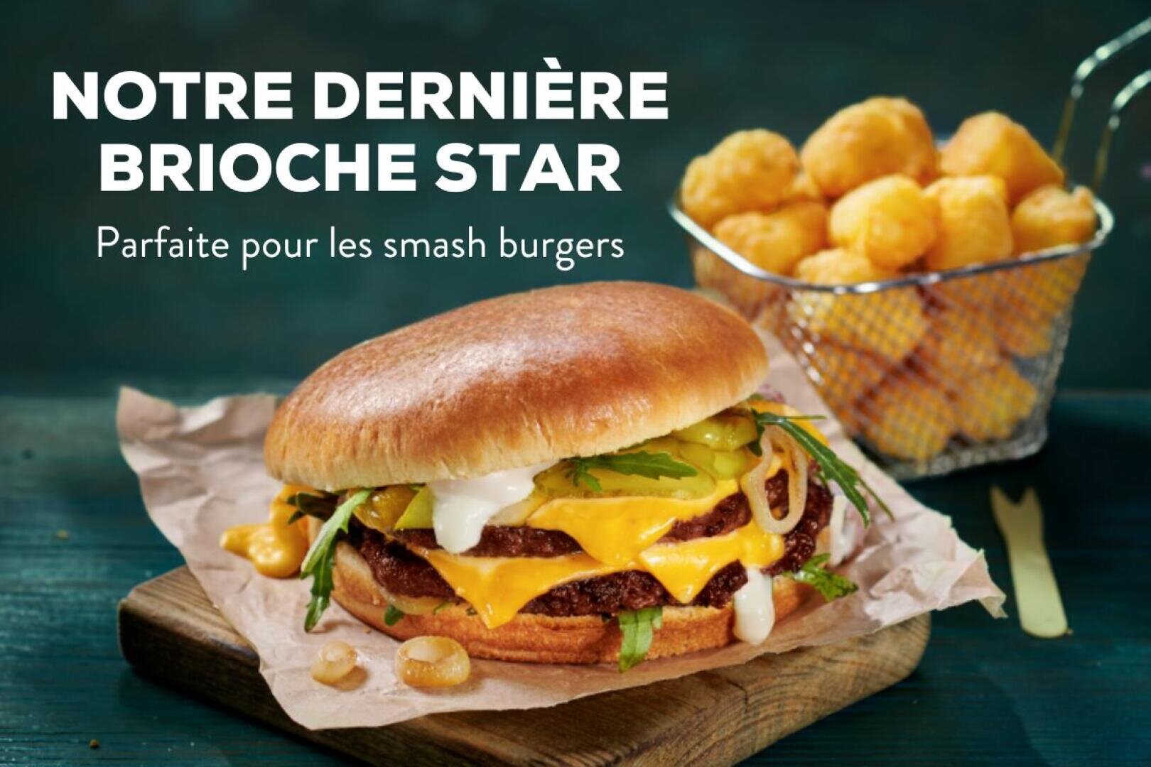 Un cheeseburger avec cornichons, oignons et sauce sur un pain brioché est posé sur du papier à côté d'un panier de croquettes de pommes de terre. Le texte ci-dessus indique : NOTRE DERNIÈRE BRIOCHE STAR. Parfaite pour les smash burgers.
