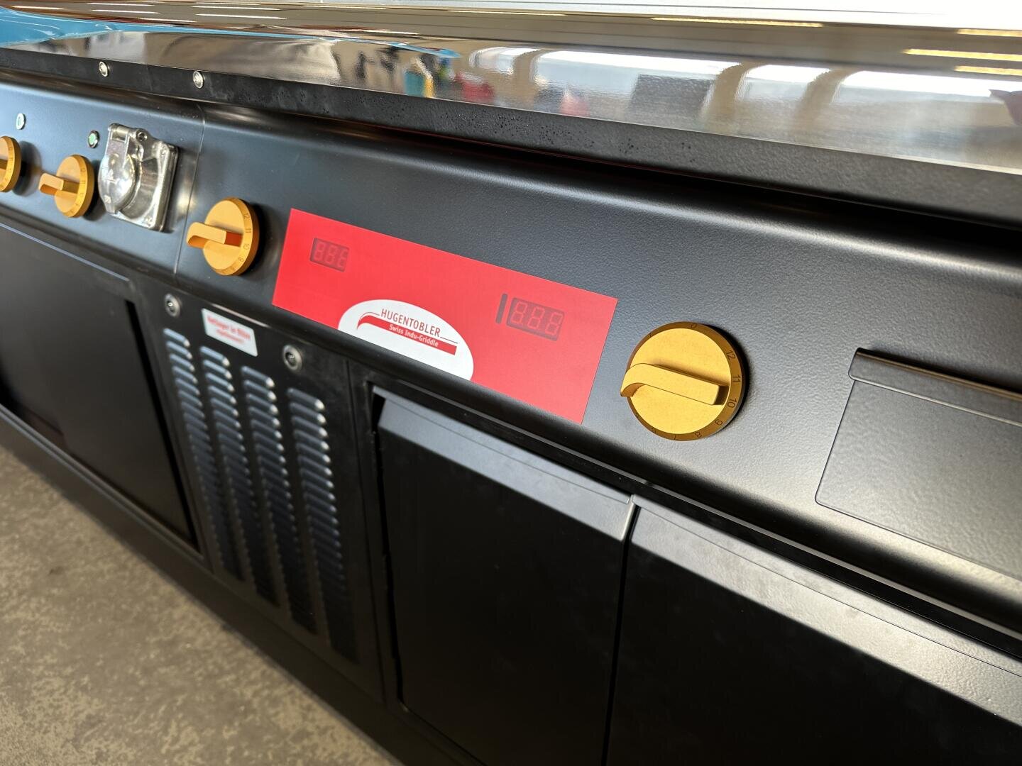 Nahaufnahme eines gewerblichen Küchengeräts mit gelben Knöpfen, digitalen Anzeigen, einem roten Etikett und schwarzen Metallplatten, das wahrscheinlich zum Kochen oder Backen verwendet wird.