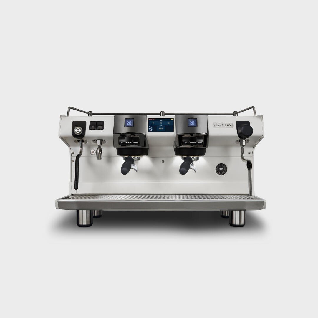 Eine moderne gewerbliche Espressomaschine mit zwei Gruppenköpfen, einer Digitalanzeige, Dampfstäben und einem Gehäuse aus Edelstahl, von vorne gesehen vor einem schlichten weißen Hintergrund.