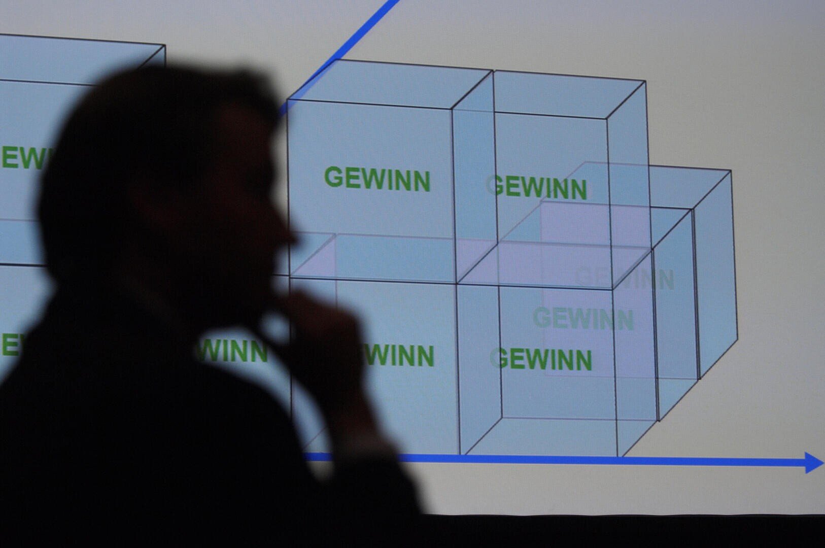 Eine Person in Silhouette betrachtet eine Präsentationsfolie mit transparenten 3D-Würfeln mit der Aufschrift GEWINN auf weißem Hintergrund mit blauen Linien und Pfeilen.