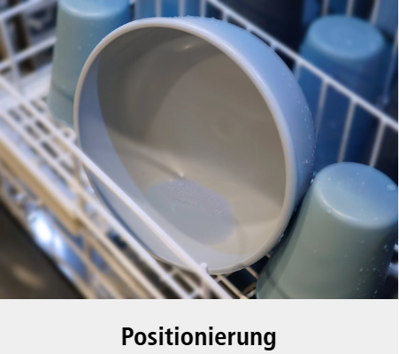 Eine hellblaue Schale, die schräg auf einem Geschirrspülergestell steht, umgeben von mehreren umgedrehten Tassen. Unter dem Bild erscheint das Wort Positionierung.