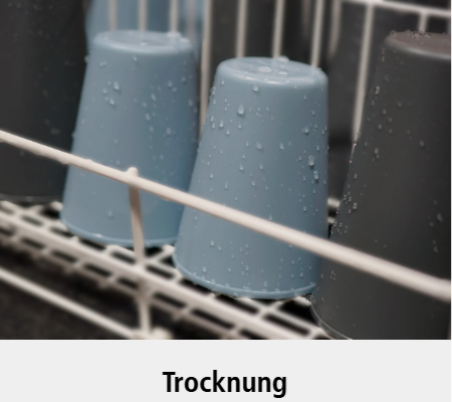 Mehrere Plastikbecher, die kopfüber in ein Geschirrspülmaschinengestell gestellt werden, mit sichtbaren Wassertropfen auf ihrer Oberfläche. Unter dem Bild steht das Wort "Trocknung".
