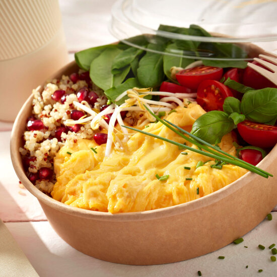 Eine Schale mit Rührei, Kirschtomaten, frischem Spinat, Quinoa, Granatapfelkernen, Bohnensprossen und Kräutern, die mit einer Plastikgabel ordentlich angerichtet ist.