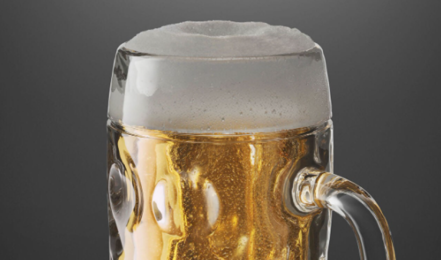 Gros plan d'une chope de bière en verre remplie de bière dorée et surmontée d'une mousse blanche, sur un fond gris uni.