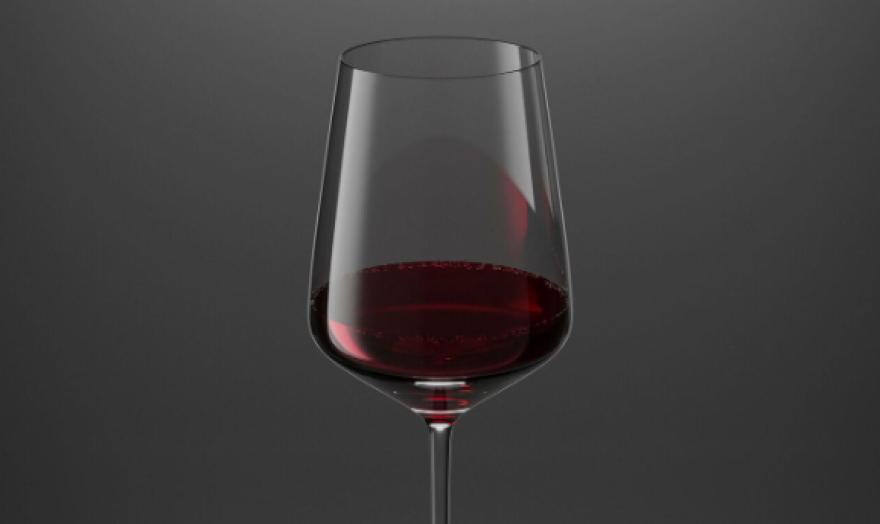 Un verre de vin rouge, à moitié plein, sur un fond gris foncé uni.