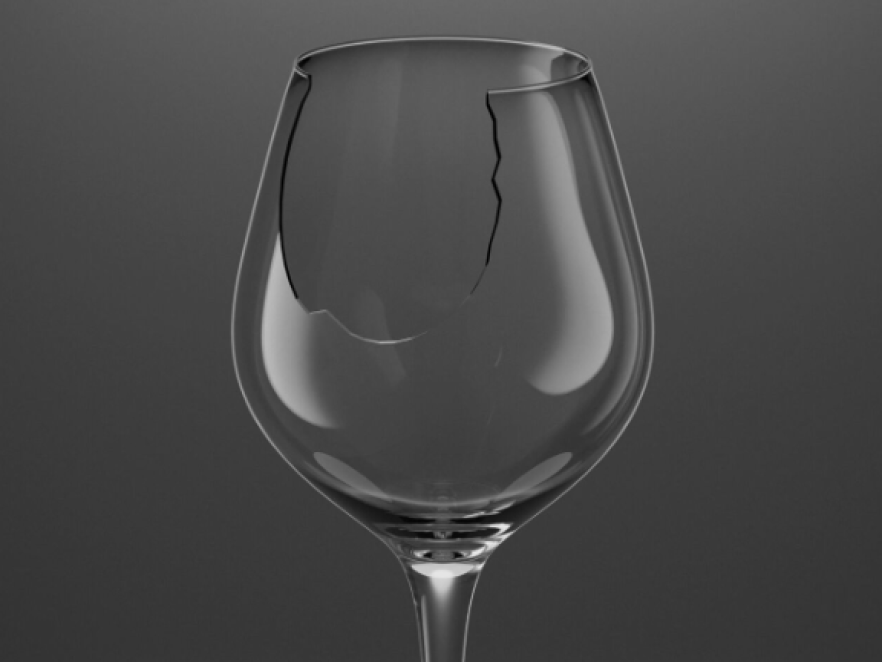 Un verre à vin dont le bord est brisé par un grand morceau déchiqueté, sur un fond gris foncé uni.