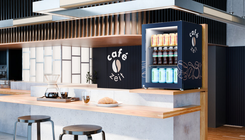 Eine moderne Café-Theke mit einer hölzernen Oberfläche, zwei Hockern, einer Kaffeemaschine, Tassen und Croissants; eine kleine Kühlvitrine mit Getränken und das Café-Logo mit der Aufschrift "café xei" an der Wand.