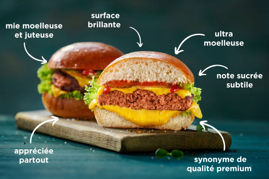 Deux burgers garnis de laitue, de fromage et de steaks végétaux, servis sur des pains brillants, sont posés sur une planche de bois. Les étiquettes françaises soulignent la douceur, la jutosité, la douceur, la surface brillante et la qualité supérieure des pains.