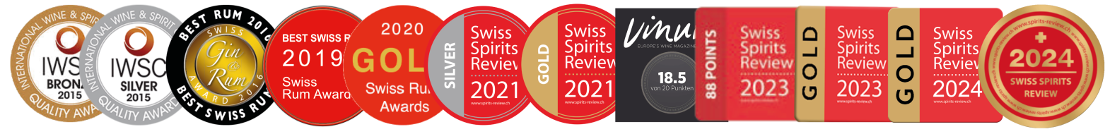 Eine Reihe von zehn Medaillen und Anstecknadeln in Gold, Silber, Bronze, Rot und Schwarz, jeweils beschriftet mit verschiedenen Jahreszahlen und der Schweizerischen Spirituosen-Revue, stehen für die Erfolge bei Spirituosenwettbewerben von 2015 bis 2024.